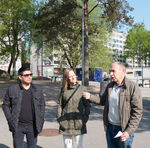 Tre personer med träd och byggnader i bakgrunden. Foto.