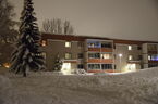 Snötäckt gräsmatta med hus i bakgrunden. Foto.